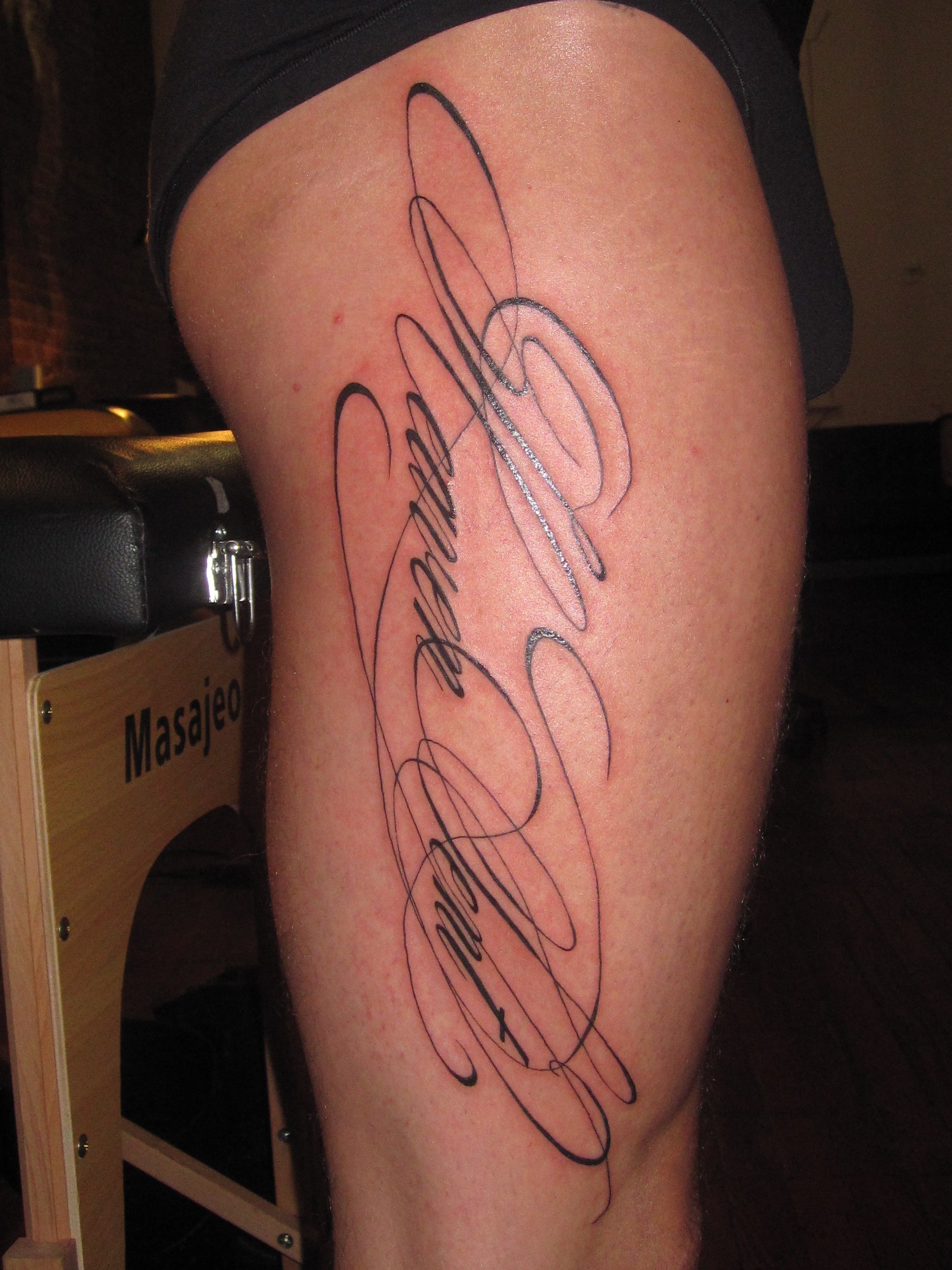 Tattoo on a person's thigh with cursive calligraphy text