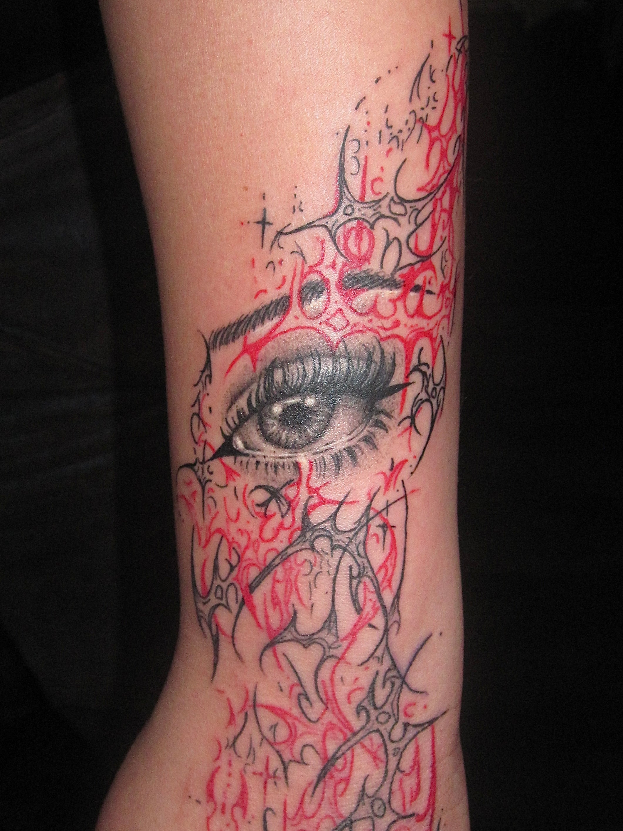 Tattoo of an eye with intricate red and black cyber sigilism design on a person's arm 